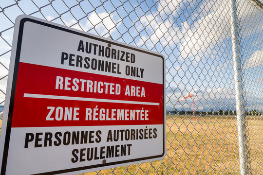 Restricted area sign on an airport fence with a windsock in the background.