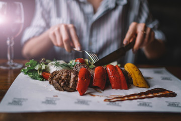 Spicy grilled lamb leg with vegetables and herbs on a roasting cast iron. Barbecue lamb with vegetables. Healthy food. Eating and leisure concept. Woman having dinner at table with food. Toned image.