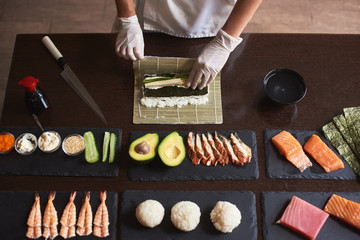 Master making a sushi roll with nori, rice, cucumber and omelet using bamboo mat. Closeup view of process. View from the top