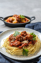 The homemade italian pasta or spaghetti with meatball , cheese and tomato sauce placed in a white dish with on dark blue tablecloth on the table..