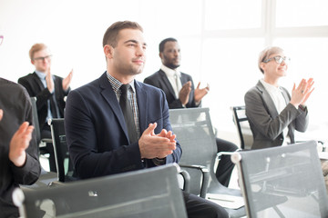 Elegant businesspeople gathering on convention and giving applause while sitting in hall and looking away