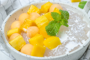 The thai dessert food modern style : The homemade sago in coconut milk with topping is mango cut into squares and cantaloupe ball in the white bowl and placed on tablecloth plaid on the marble table.