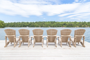 Row of Muskoka chairs on a dock looking onto the lake.