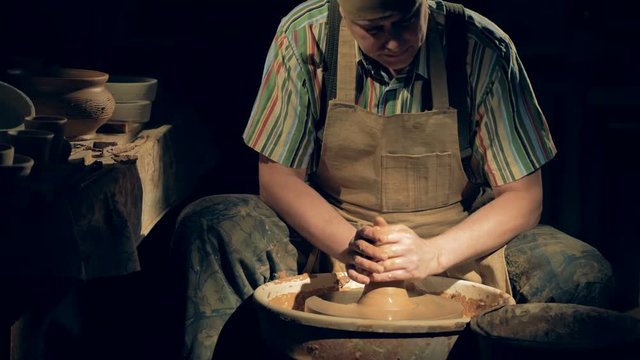 A potter works with clay on a wheel.