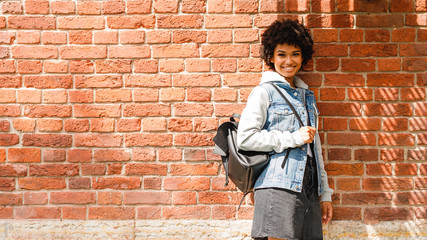 Fototapeta na wymiar Smiling teenage girl standing at brick wall