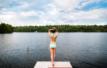 Young woman standing on a dock with geese on a lake.