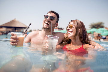 Happy young couple drinking lemonade in swimming pool