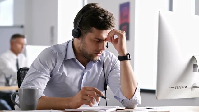 Young bored handsome man working in call center and talking in headphones in  office