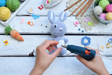 Making rabbit with carrot. Crochet bunny for child. On table threads, needles, hook, cotton yarn. Step 3 - glue eyes of toy. Handmade crafts. DIY concept. Small business. Income from hobby.