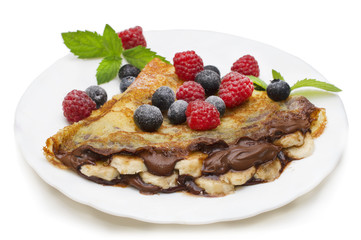 Homemade crepes served with chocolate cream, fresh blueberries and raspberries, powdered sugar on a white background