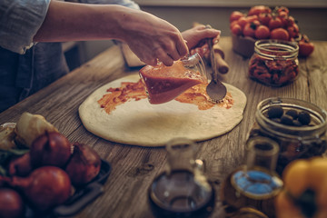 Fresh original Italian raw pizza and ingredients on wooden table, preparation in traditional style. Woman cooking homemade pizza on a wooden table in a home kitchen. Cooking, food and people concept.
