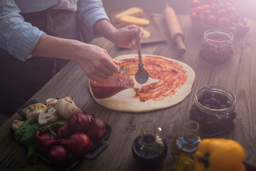 The process of making pizza. Prepare dough hand topping. Woman hand is spreading pasteurized tomato paste onto a pizza base. Food concept. Preparing traditional italian pizza. Toned image.