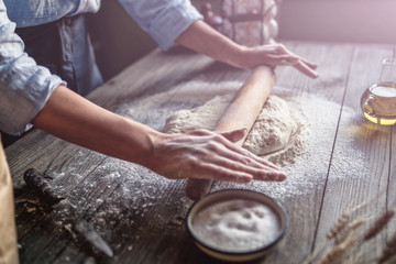 Pizza dough with ingredients on rustic wooden table. Woman hands keep rolling pin with flour on dark brown table, baking background, menu, recipe. Preparing bread dough on wooden table in a bakery.