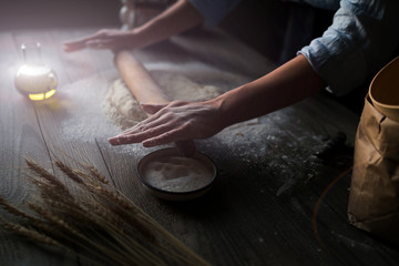 Fototapeta na wymiar Pizza dough with ingredients on rustic wooden table. Woman hands keep rolling pin with flour on dark brown table, baking background, menu, recipe. Preparing bread dough on wooden table in a bakery.