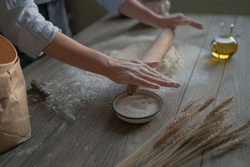 Homemade raw dough on a rustic wooden table. Making pizza. Dough with a rolling pin. Flour, butter, wheat spikelets. Concept of cooking and food. Toned image.