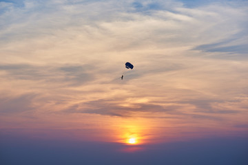 Sunset over the ocean. Silhouette of a lonely parachute on sunset background. Sky, clouds and water. Beautiful serene scene. Natural composition of nature. Landscape. Concept of outdoor activities.