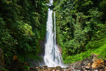 Naklejka na ściany i meble Beautiful waterfall in green tropical forest. View of the falling water with splash of water makes. Nature landscape. Morning view on hidden majestic waterfall in the deep rain forest jungle. .