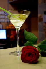 Cocktail with alcohol and two olives on a stick on the bar table with a red rose
