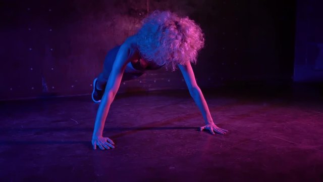 Attractive young woman with long curly hair wearing shorts and sports bra doing push ups in a dark gym. Slider slow motion medium shot