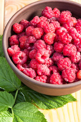 Fresh organic healthy raspberry with mint leaves in clay dish on wooden table background. Rustic style and natural light. food photo.