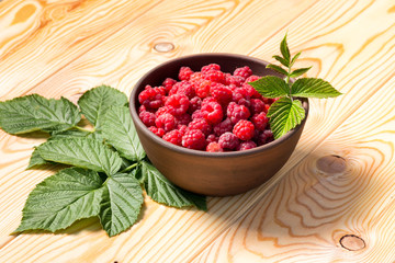 Fresh organic healthy raspberry with mint leaves in clay dish on wooden table background. Rustic style and natural light. food photo.