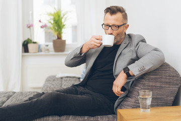 mann sitzt auf dem sofa und trinkt eine tasse kaffee