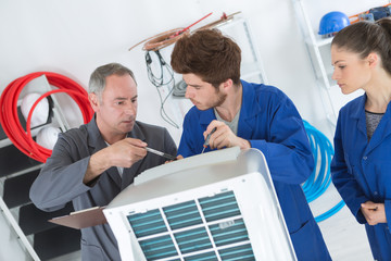 technician is checking air conditioner with apprentices