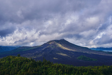 Fototapeta premium Tło podróży. Wiejski wschód słońca krajobraz. Wieś i zielony las tropikalny. Naturalne tło. Krajobraz wulkan Batur na wyspie Bali, Indonezja. Dramatyczne niebo z chmurami w górach.