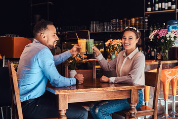 Happy beautiful African-American couple in love having a great time together in a restaurant at their dating, an attractive couple enjoying each other, holds glasses of juice.