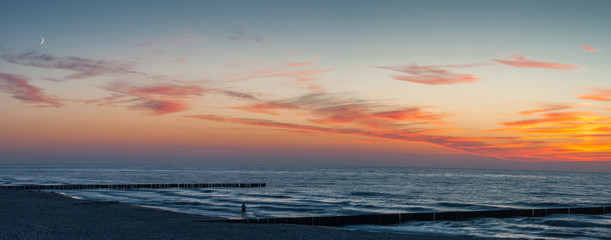 Panoramic sunset and a single person walking along the seashore