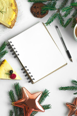 Blank open notepad, pine branches and Christmas decorations on a white table. cheesecake, stars, notebook, christmas tree on a white background Space for text. Top view. Flat lay style.