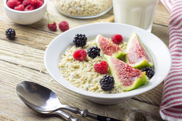Bowl of oatmeal porridge with figs, raspberries and blackberries on teal rustic table, hot and healthy food for Breakfast, top view, flat lay