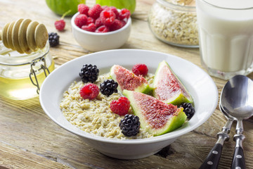 Bowl of oatmeal porridge with figs, raspberries and blackberries on teal rustic table, hot and healthy food for Breakfast, top view, flat lay