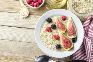 Bowl of oatmeal porridge with figs, raspberries and blackberries on teal rustic table, hot and healthy food for Breakfast, top view, flat lay