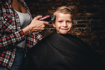 Happy preschooler boy getting haircut. Children hairdresser with the trimmer is cutting little boy in the room with loft interior.