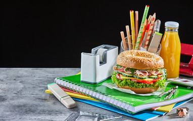 Burger and orange juice bottle on school supplies