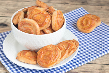 Homemade snail shaped cheese snack on blue checkered table cloth in white bowl.