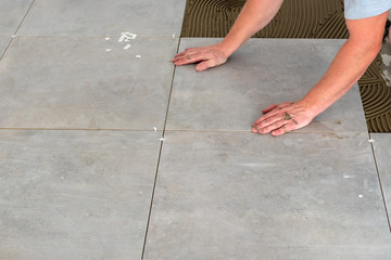The hands of the tiler are laying the ceramic tile on the floor.