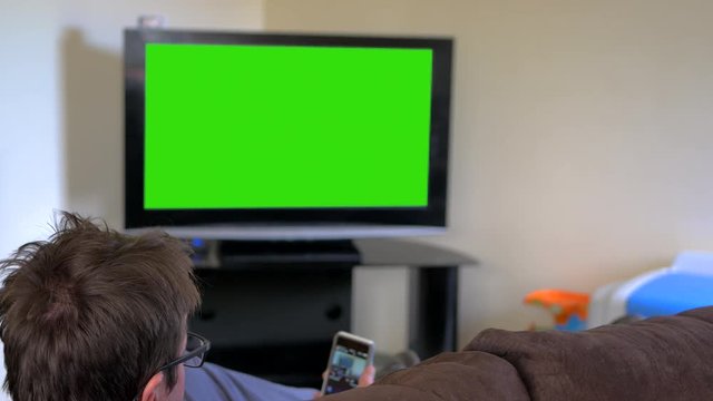 Man watching television and checking smart phone. Green screen and rear view.