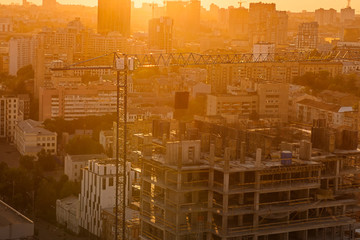 Construction crane and buildings under construction in urban city scape in back sunset light. Residential or business infrastructure development and expansion of the city. Selective focus, copy space.