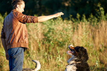 the guy is walking with a dog in the countryside. feeds and trains. the dog jumps for the delicious