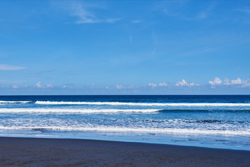 Black sand volcanic beach with waves and deep blue ocean. Summer tourism and holiday concept. Blue sea water and blue sky. View amazing nature background. Exsotic landscape with copy space..