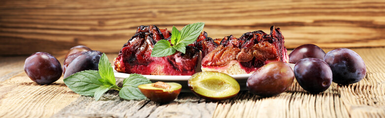 Rustic plum cake on wooden background with plums around.