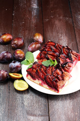Rustic plum cake on wooden background with plums around.