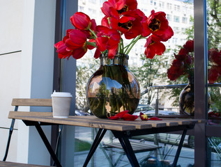 vase with tulips and a paper cup with coffee street restaurant