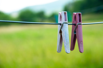Two old worn pink clothes pegs hang on metal wire. Old clothespins on shiny wire. On a blurred green background. A clothesline with two clothespins on the street.