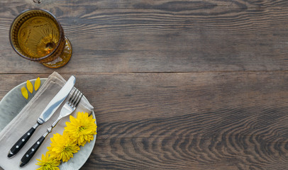 Rustic table setting with linen napkin, cutlery, ceramic plates, yellow glasses and yellow flowers