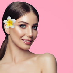 Fototapeta na wymiar Attractive spa woman with perfect healthy skin and tropic flower on pink background. Facial treatment, cosmetology and spa