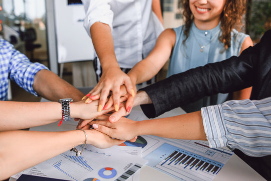 Entrepreneurs Folded Their Hands Together Sitting At A Table In The Office Close-up, The Concept Of Team Spirit Of Young Creative People