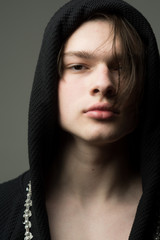 Fototapeta premium Macho in black bathrobe with hood, close up. Guy on confident face in black hood, grey background. Masculinity concept. Man with smooth skin on face and neck looking at camera.